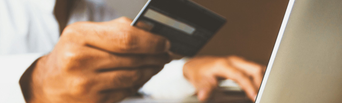 man holding credit card while entering the information on a laptop