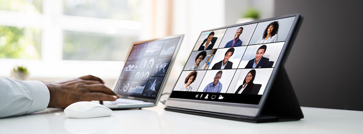 freelance gig worker typing on laptop while participating in a conference video call on tablet
